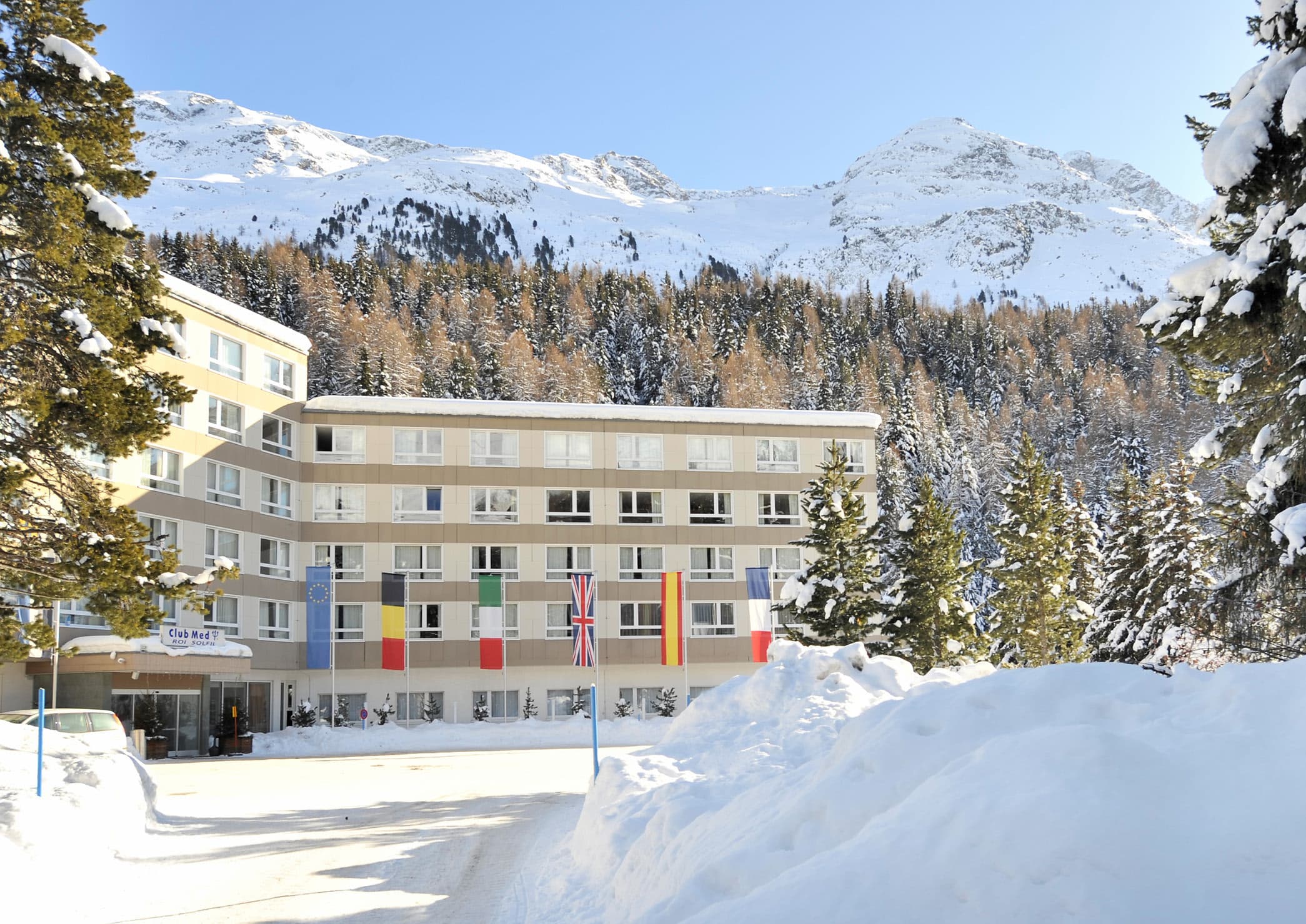 Club Med Saint-Moritz Roi Soleil under fresh snow, the Engadine peaks rising behind the fir forest