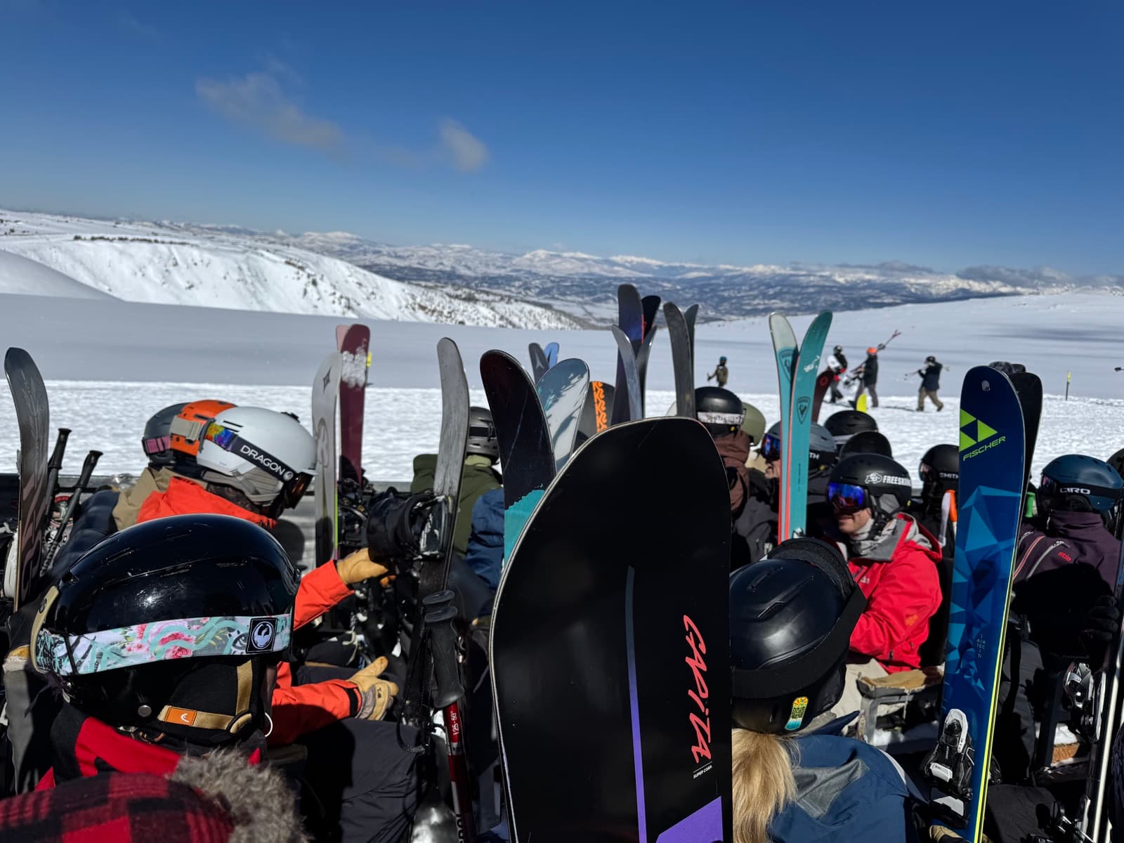 A ski crew gathered at the summit, skis and boards up, mountains behind