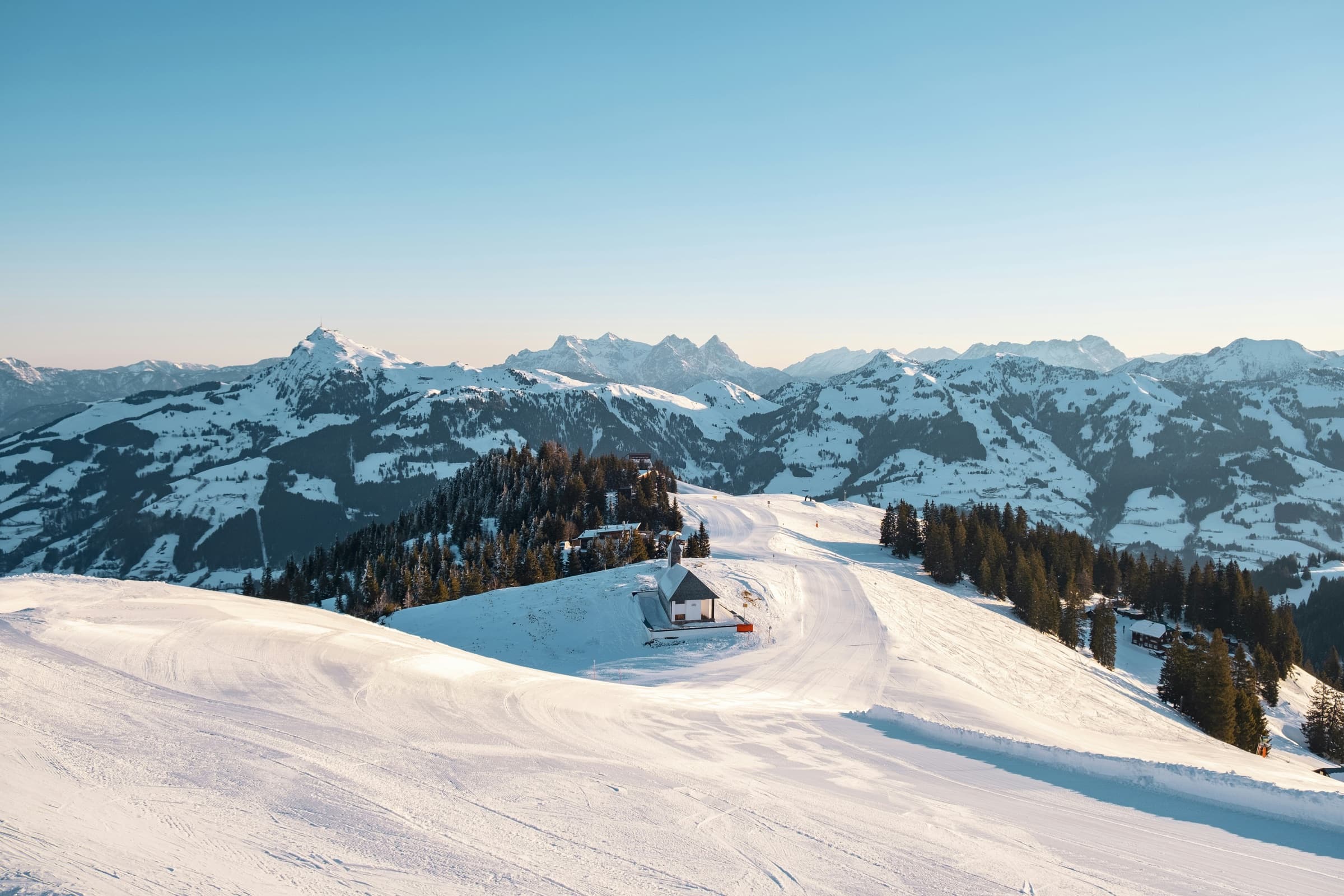 Golden-hour panorama over the Kitzbühel ski area, with a mountain hut and the Tyrolean Alps beyond