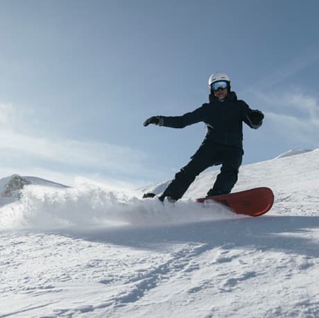A snowboarder throwing up spray on a sunlit Engadine slope