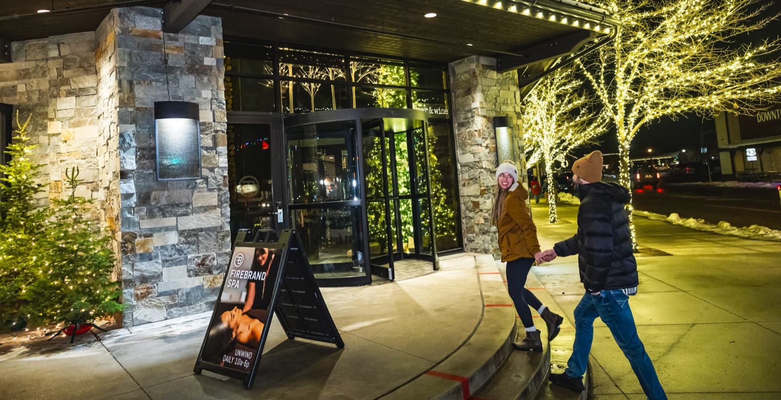 A couple heading into The Firebrand Hotel past trees wrapped in warm white lights