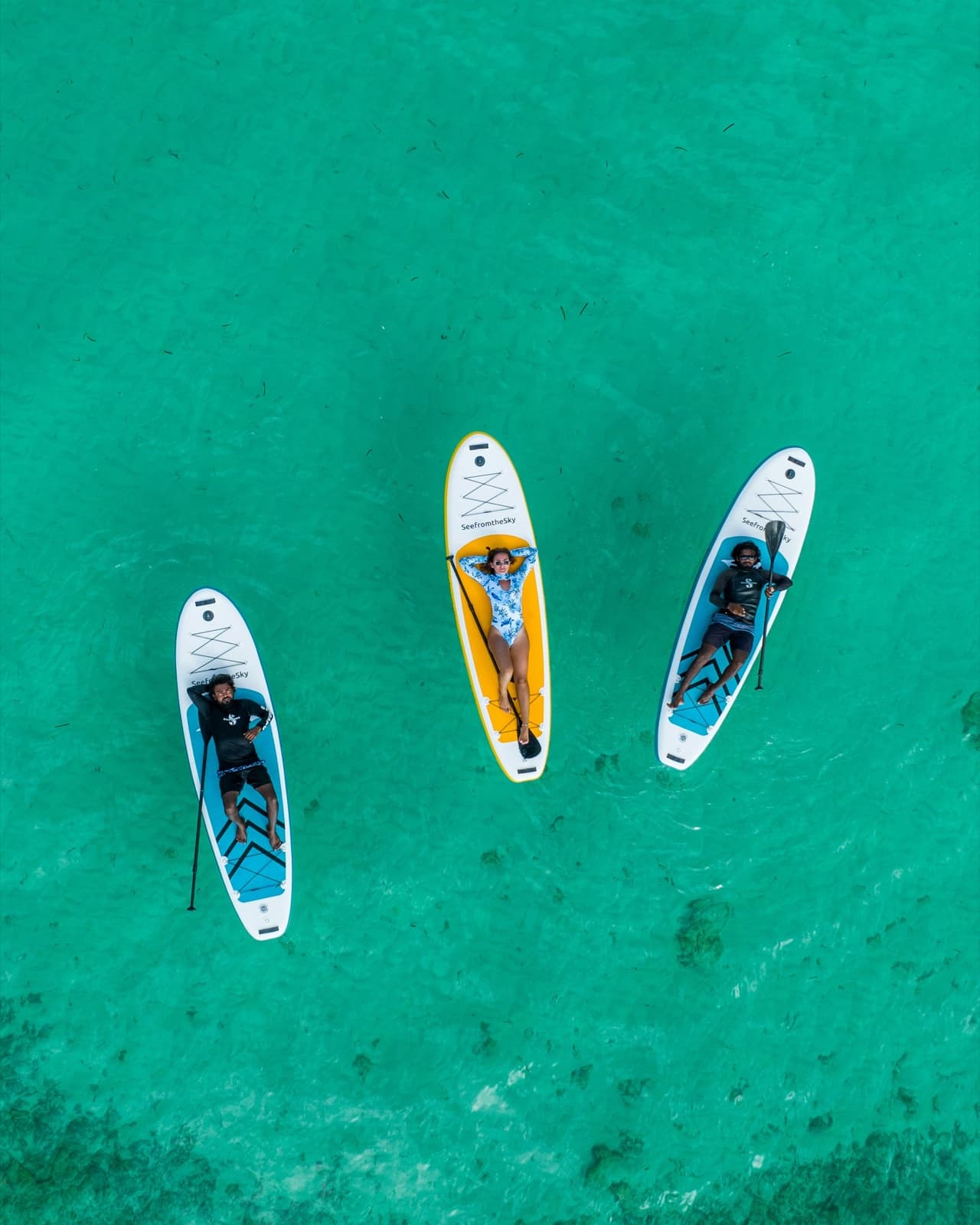 Paddleboarders on clear turquoise water, seen from above