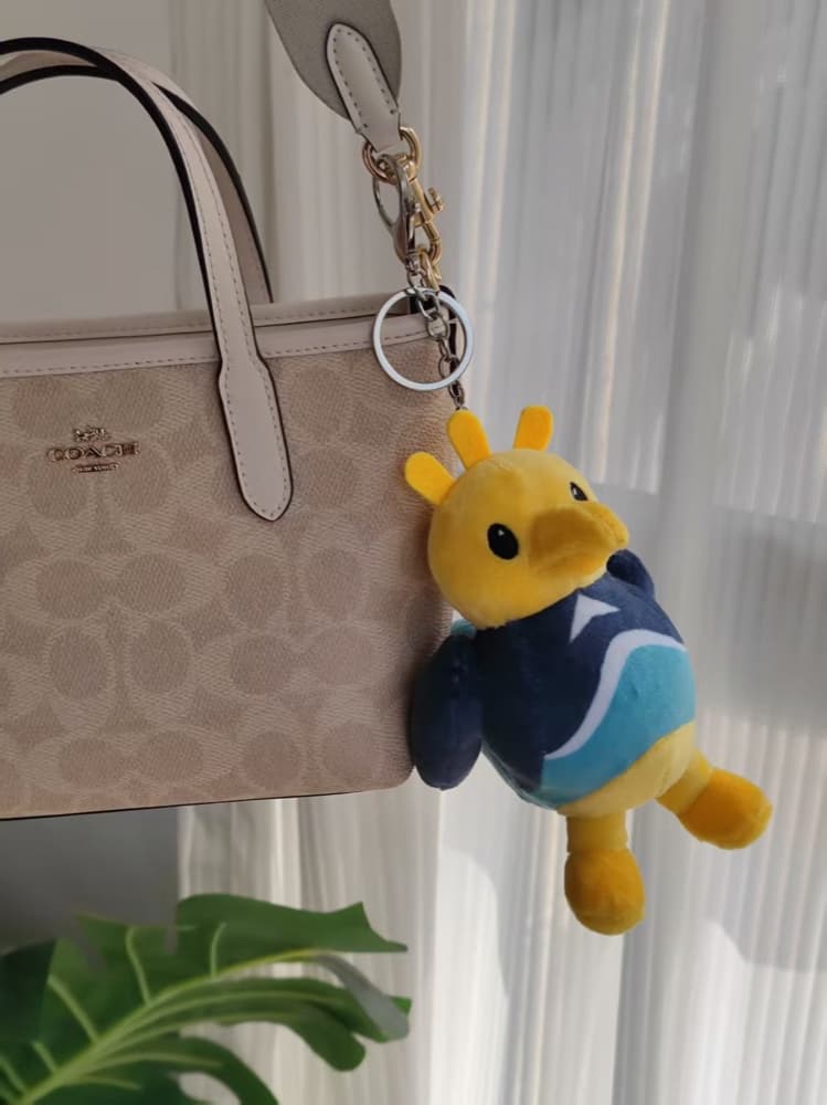 The real Sandigo plush keychain clipped to a travel bag