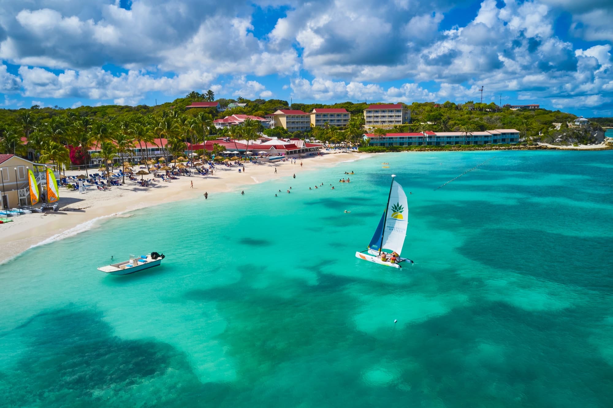 Aerial view over Pineapple Beach Club — white sand, a Hobie-cat sailboat, and turquoise Caribbean water in Antigua